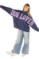 A woman modeling an oversized navy blue sweatshirt with 'DOG LOVER' printed across the front in pink glitter-style lettering, paired with light-wash wide-leg jeans and white sneakers on a white background.