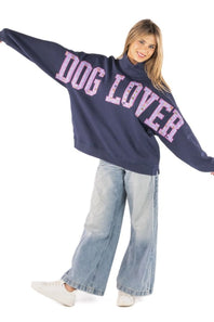 A woman modeling an oversized navy blue sweatshirt with 'DOG LOVER' printed across the front in pink glitter-style lettering, paired with light-wash wide-leg jeans and white sneakers on a white background.