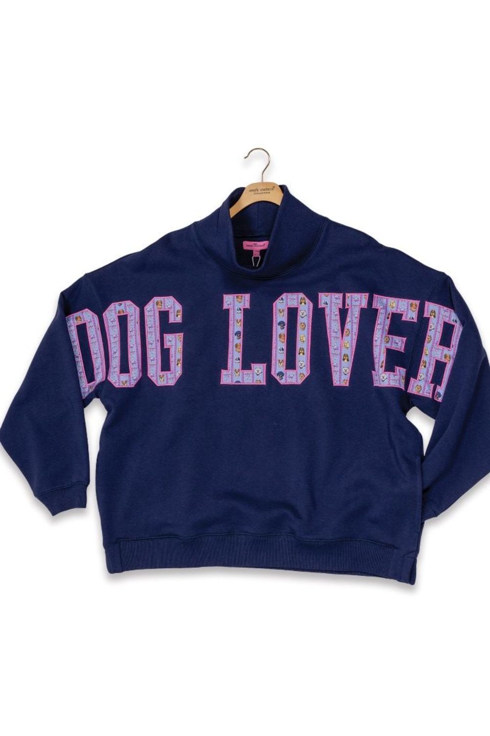 A navy blue mock-neck sweatshirt with 'DOG LOVER' printed across the chest in pink and purple patterned letters, hanging on a wooden hanger against a white background.