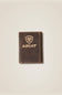 A dark brown textured leather card holder wallet with gold-toned stitching and an embossed Ariat shield logo and brand name on the front, set against a light beige background.