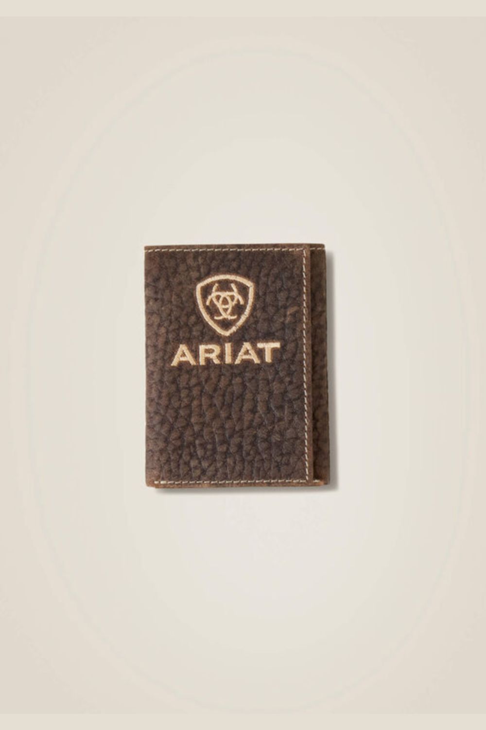A dark brown textured leather card holder wallet with gold-toned stitching and an embossed Ariat shield logo and brand name on the front, set against a light beige background.