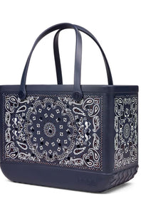 A navy blue tote bag featuring a white paisley bandana print on the front and sides, with matching dark handles and a quilted base.