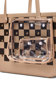 A beige tote bag with a black and beige checkerboard pattern, featuring a clear plastic zippered pouch with white polka dots and a smaller matching clear pouch attached to the front.