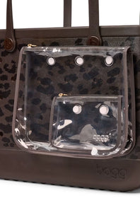 A close-up of a brown leather tote bag with a dark brown leopard print pattern and a clear plastic front pouch pocket with metal grommets. The brand name 'bogg' is embossed on the bottom right corner of the bag.