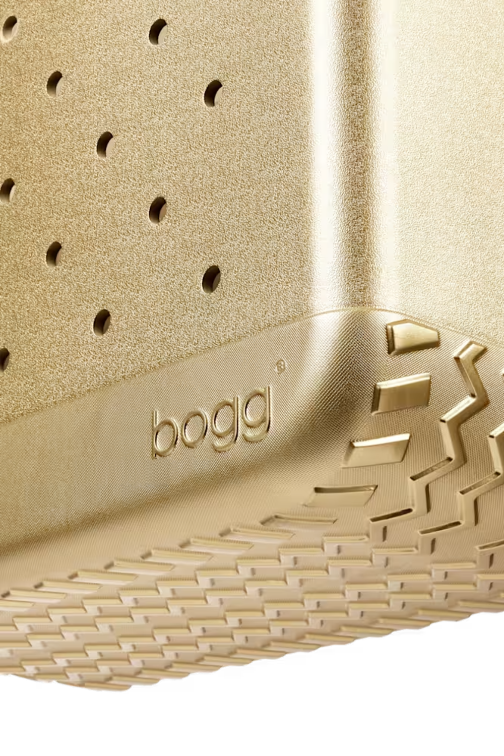 Close-up of a gold-colored Bogg brand product, showing a textured surface with a perforated top section, a treaded bottom edge, and the embossed 'bogg' logo.