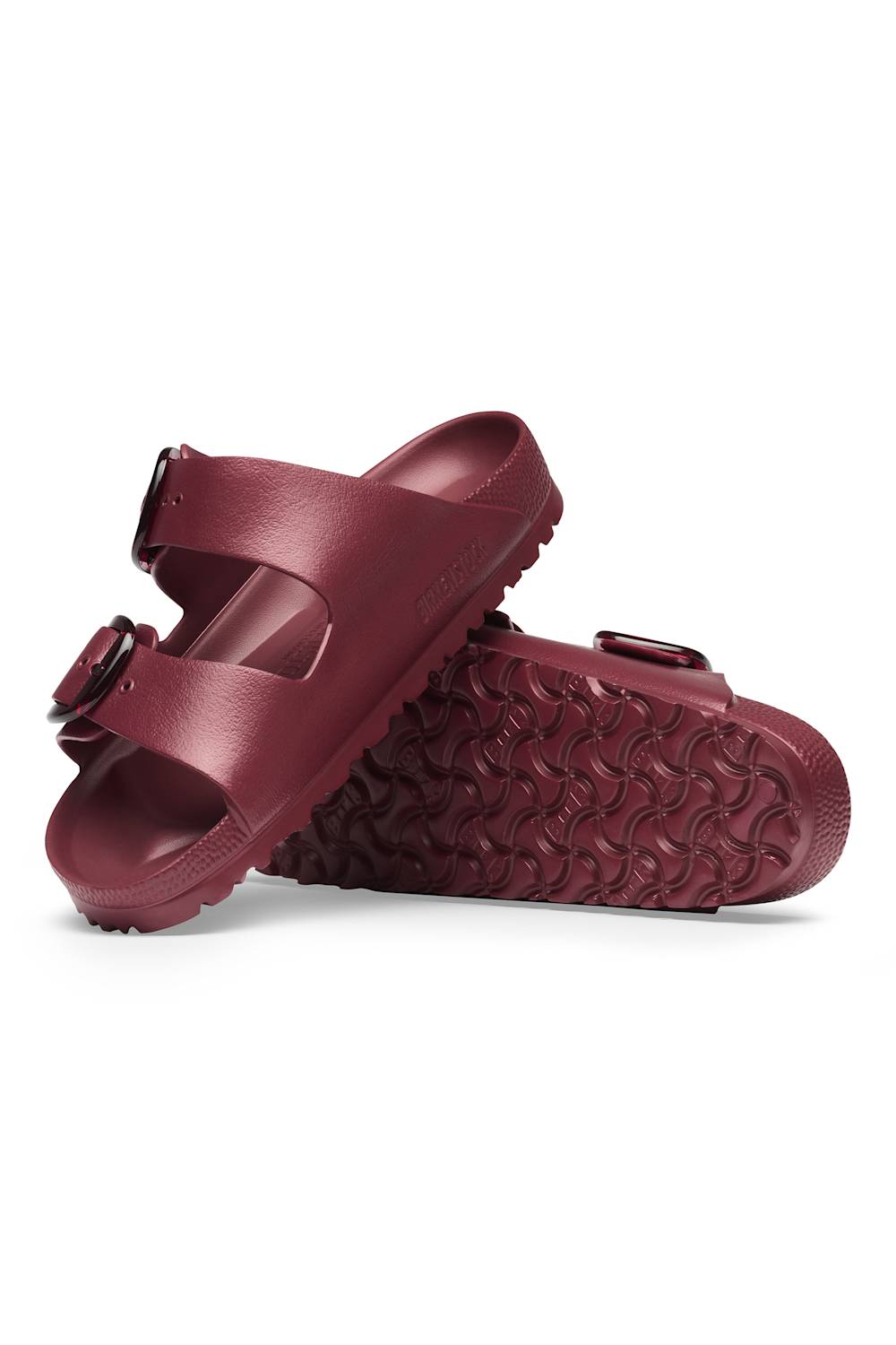 A pair of burgundy double-strap slide sandals with textured, wavy tread soles, shown from a three-quarters angle on a white background.