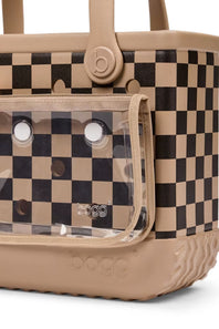 A close-up of a dog carrier bag with a beige and black checkerboard pattern, featuring a clear plastic front window and beige handles.