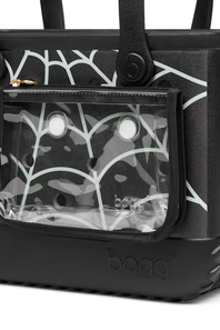 Close-up of a black Bogg tote bag with a clear front zip pocket showing a black-and-white camouflage patterned insert, plus a black handle and embossed Bogg branding on the base.