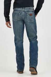 Rear view of a person wearing blue denim jeans with a dark navy shirt and brown shoes, standing against a light gray studio background.