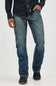 A person wearing blue denim jeans with a dark navy button-up shirt and dark slip-on shoes, shown from the chest down against a light gray studio background.