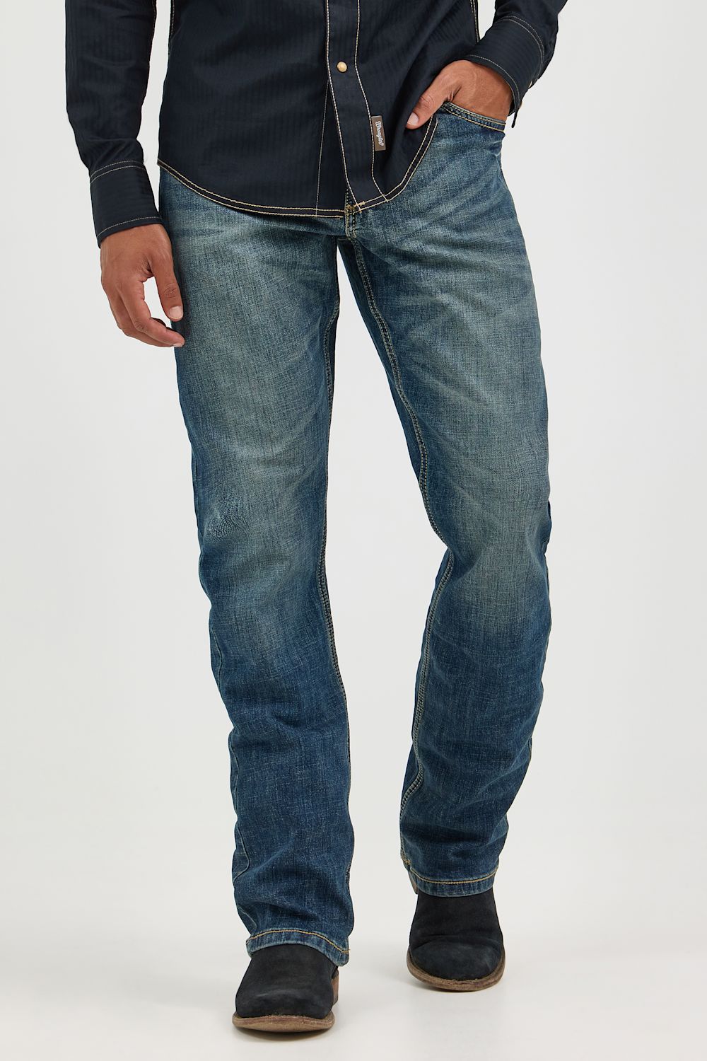 A person wearing blue denim jeans with a dark navy button-up shirt and dark slip-on shoes, shown from the chest down against a light gray studio background.