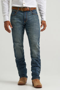 A person wearing medium-wash blue denim jeans with a brown belt and brown boots, shown from the waist down against a light gray studio background.