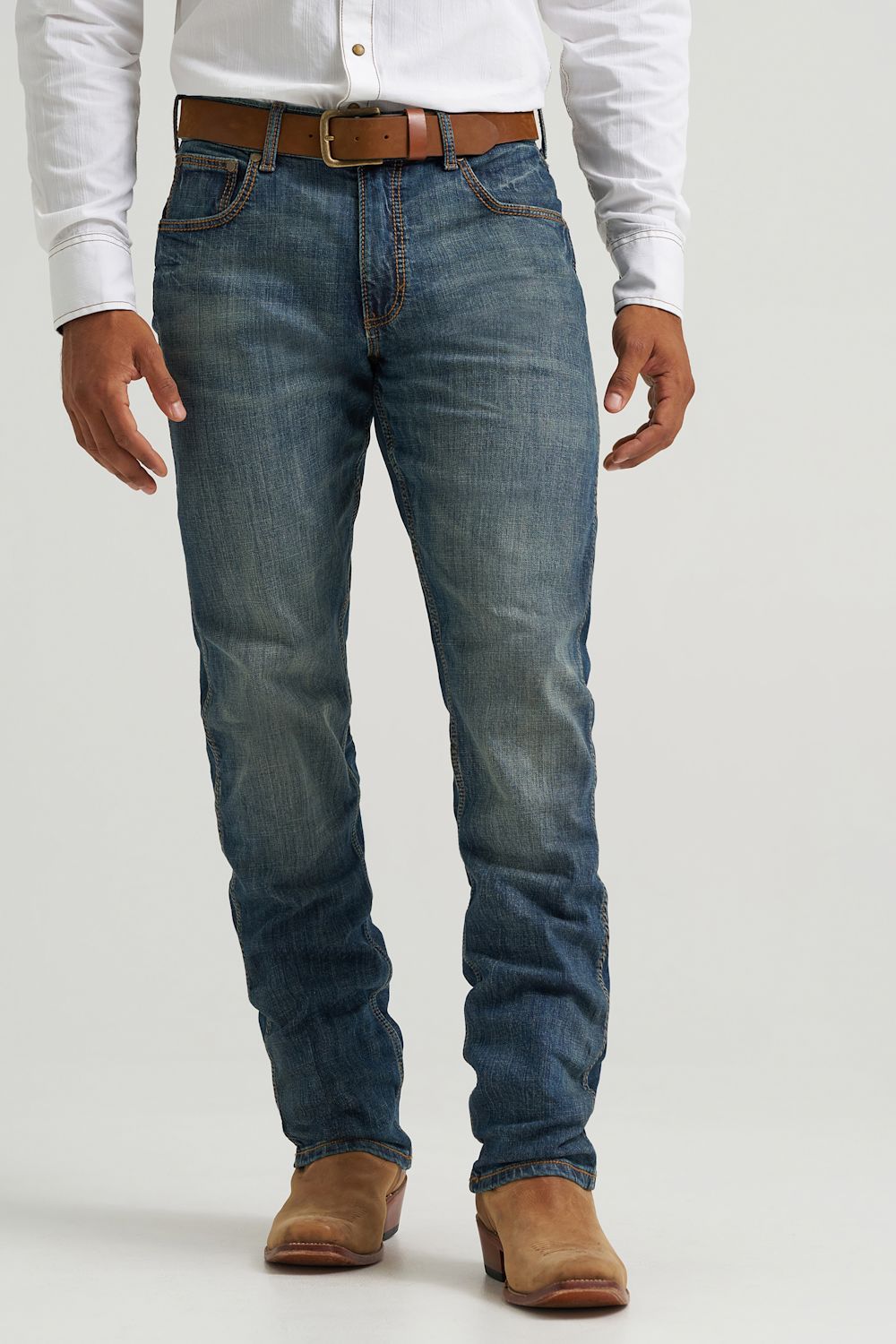 A person wearing medium-wash blue denim jeans with a brown belt and brown boots, shown from the waist down against a light gray studio background.