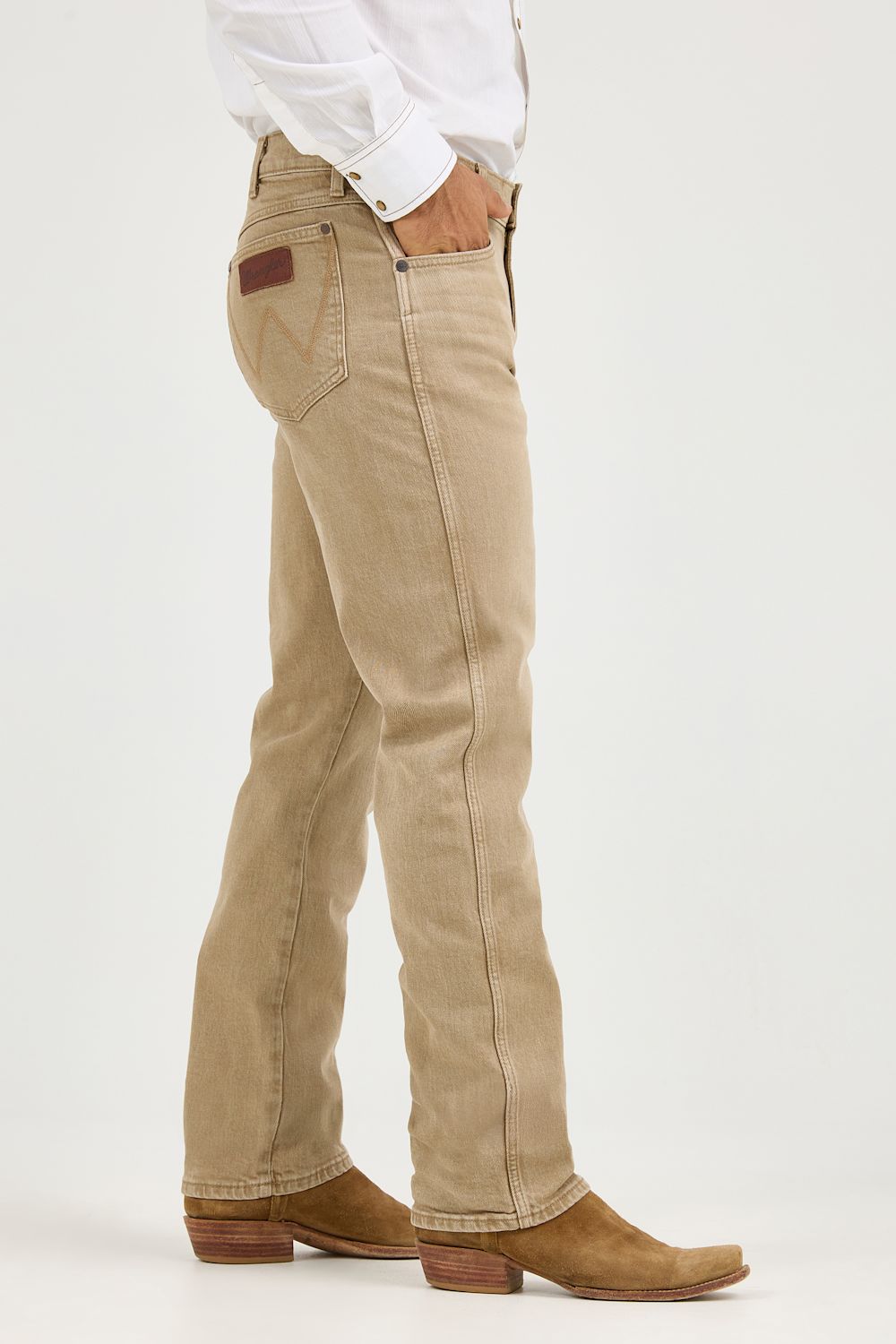 A side profile view of a person wearing beige western-style jeans, a white long-sleeve shirt, and brown cowboy boots against a plain white studio background.