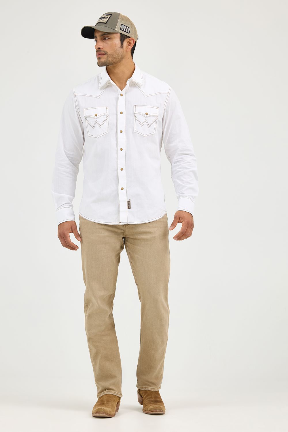 A man modeling a white long-sleeve western-style button-up shirt with embroidered chest pockets, paired with khaki pants, brown boots, and a gray baseball cap against a plain light gray studio background.