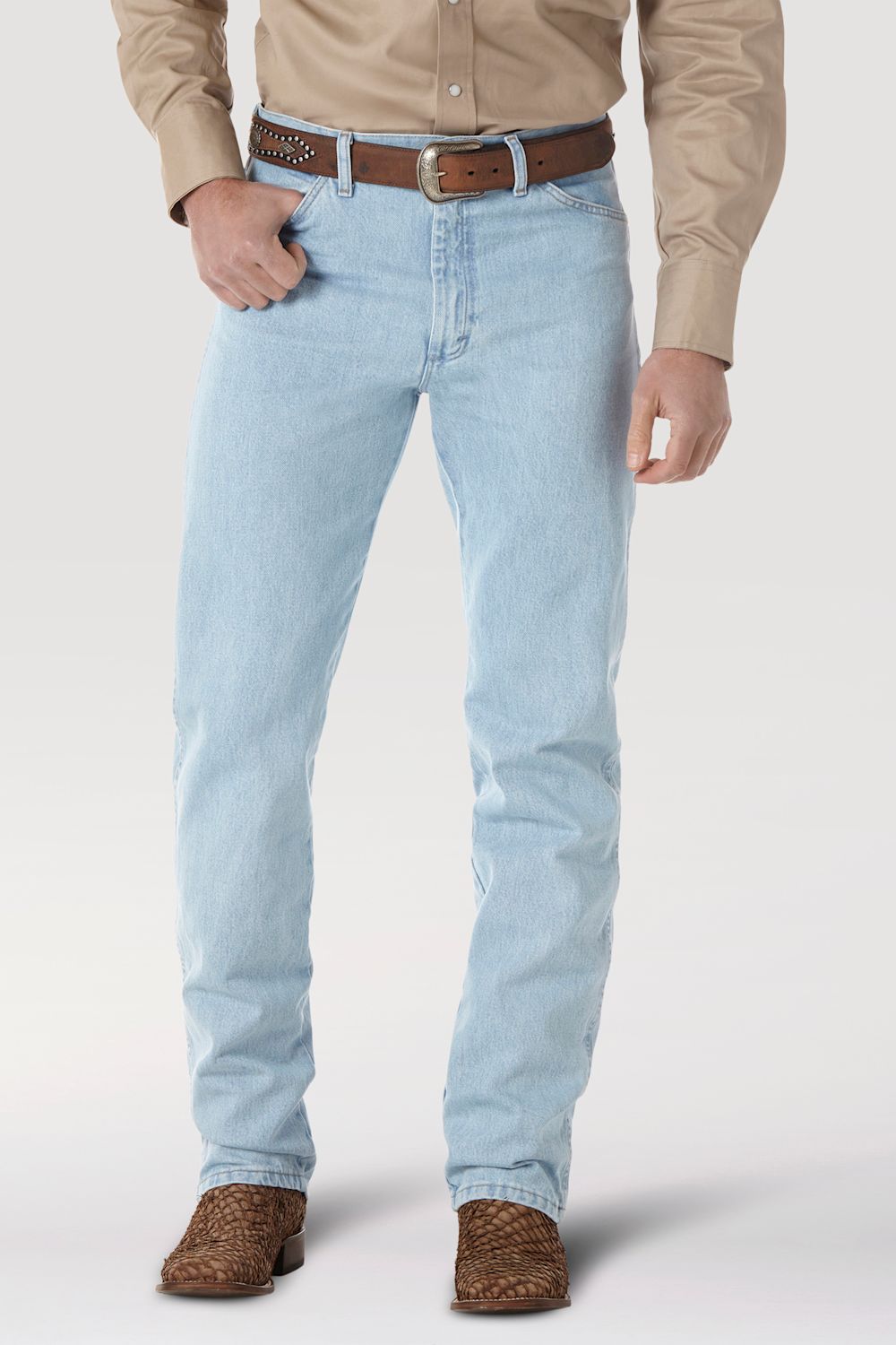 A person wearing light-wash blue jeans with a brown belt, tan button-up shirt, and brown woven shoes, shown from the waist down on a light gray studio background.