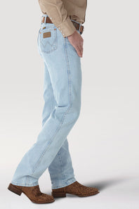 A side profile view of a person wearing light-wash blue jeans, a tan shirt, and brown cowboy boots against a light gray studio background.