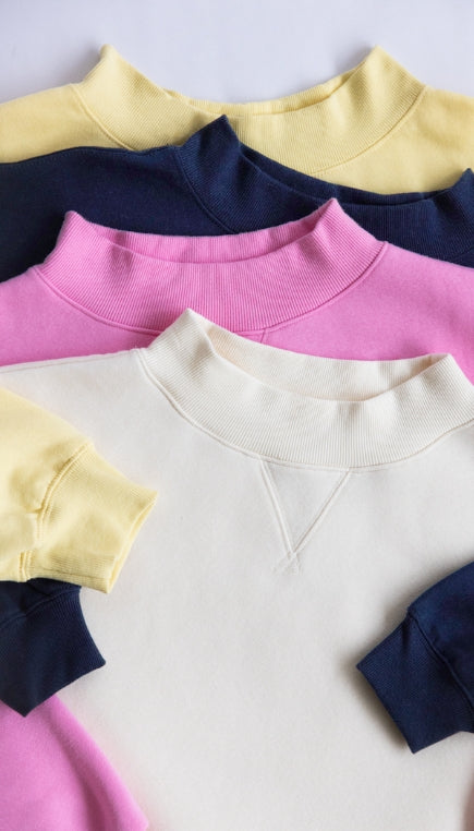 4 different mock neck sweatshirts laying staggered on top of each other, the colors top to bottom being yellow, navy, pink and beige