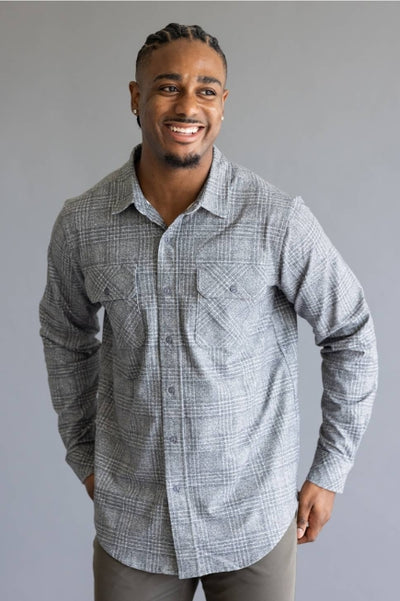 Man wearing grey and white plaid long sleeve button up shirt with dark khaki pants standing in front of a grey studio background