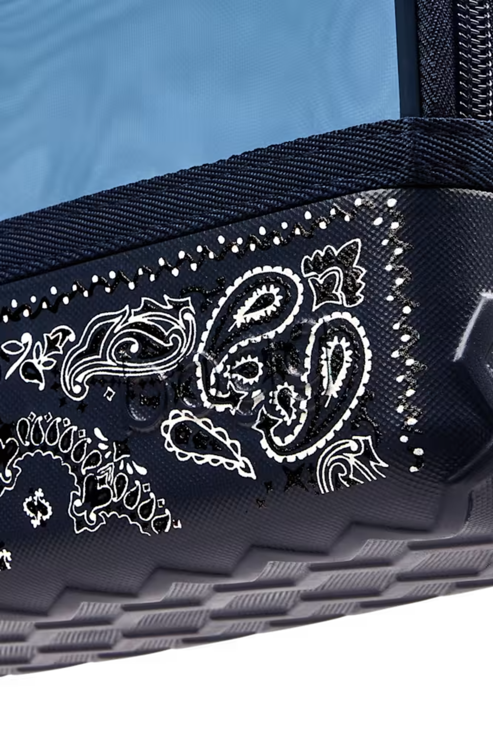 Close-up of a dark navy or black textured fabric accessory with white paisley bandana-style embroidery and dotted trim, against a light blue background.
