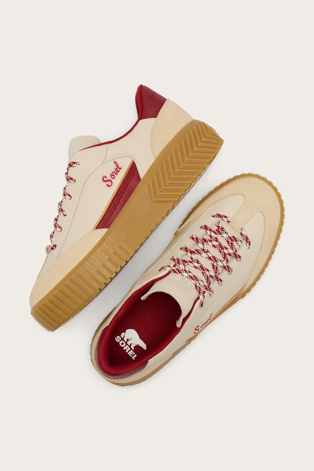A pair of low-top sneakers shown from top and side angles on a light beige background. The shoes feature cream-colored uppers with red laces, red heel tab, and red interior lining, paired with tan wavy soles and a red heel accent.