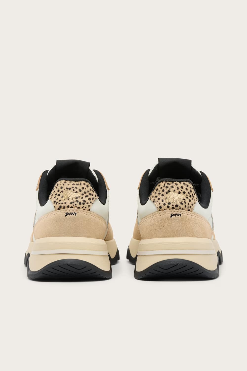 A pair of low-top sneakers shown from the back, featuring beige and cream panels, a black leopard-print heel tab, and chunky black and beige midsoles on a light gray background.