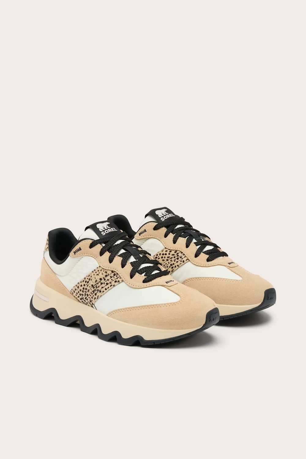 A pair of low-top sneakers in beige, white, and black, featuring a leopard-print side panel and chunky black soles, set against a light beige background.