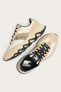 A pair of Sorel sneakers in beige and white with black accents, including a leopard print pattern on the side and a black Sorel logo on the tongue, shown on a light beige background.