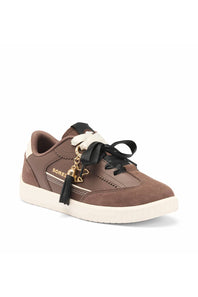 A brown suede and leather sneaker with black laces, a black tassel charm, gold-tone hardware, and a thick off-white sole. 