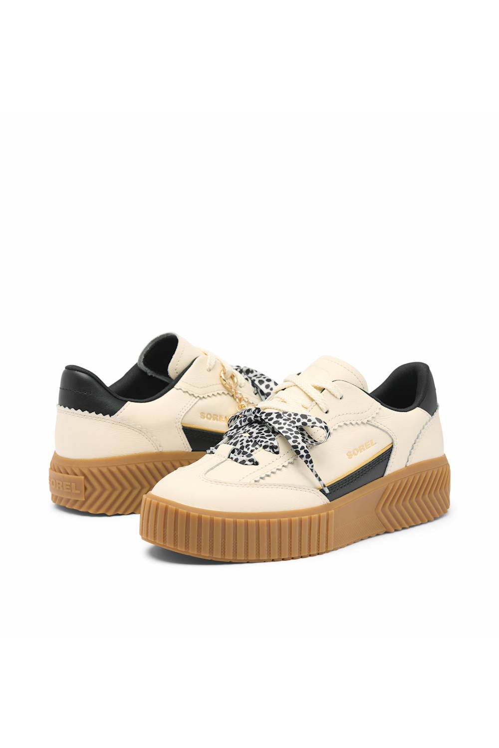 A pair of platform sneakers in cream and black with brown gum soles and patterned laces, shown on a plain white background.