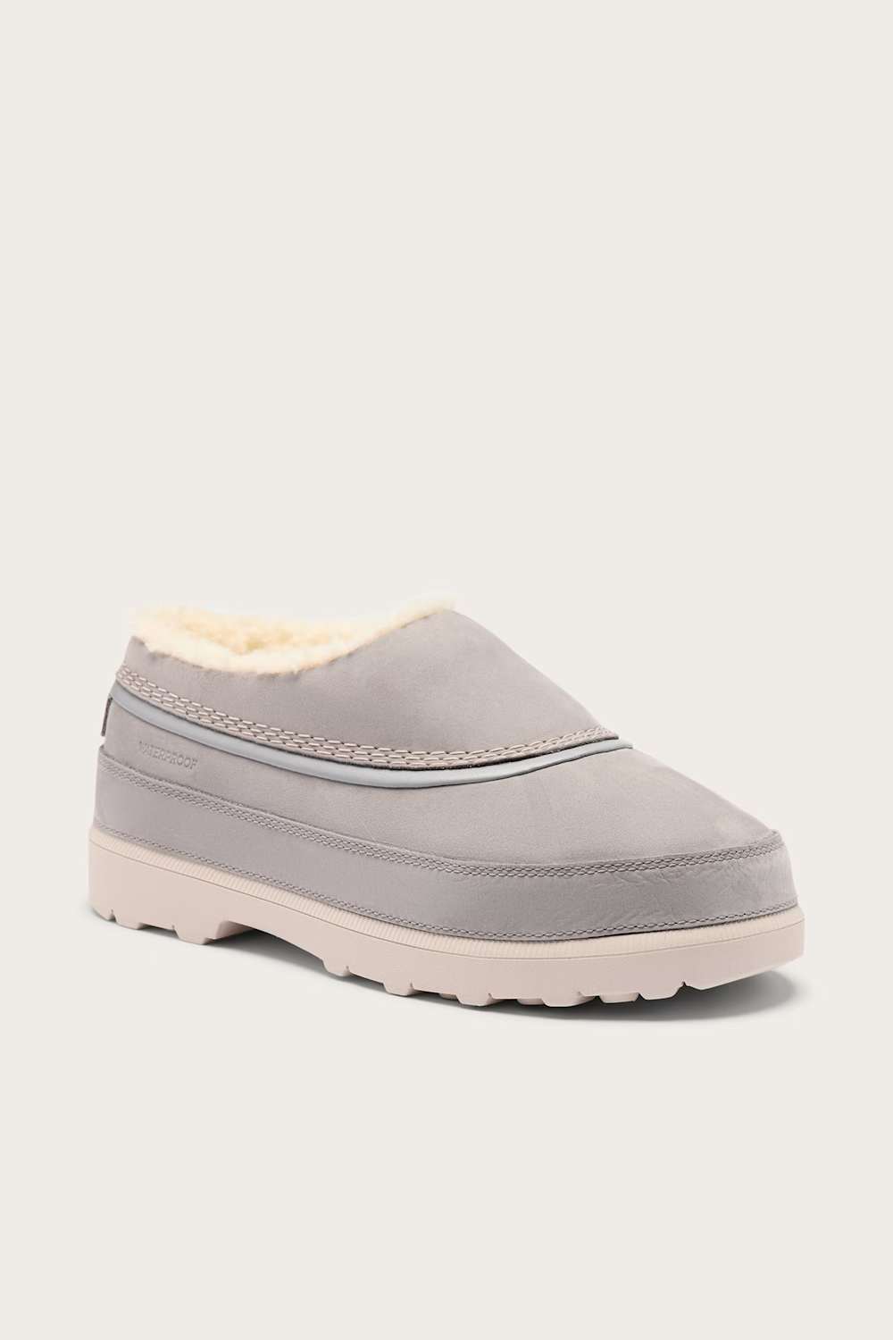 A light gray slip-on clog with a soft cream-colored shearling lining and a thick, textured off-white sole, shown against a solid light gray background.