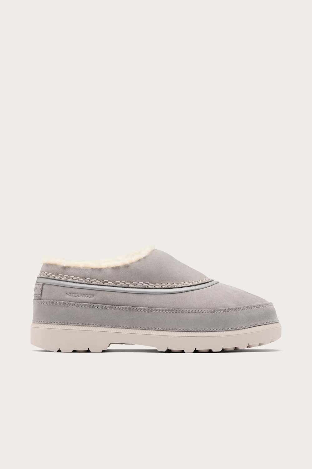A light gray slip-on clog with a soft cream-colored shearling lining and a thick, textured off-white sole, shown against a solid light gray background.