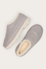 A pair of light gray slip-on clogs with cream shearling lining, shown from top and side angles on a light off-white background.