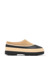 A single slip-on clog-style shoe shown in side profile on a plain white background. The upper is tan/beige with a black toe cap and black heel detail, and it has a thick beige midsole with a black outsole.