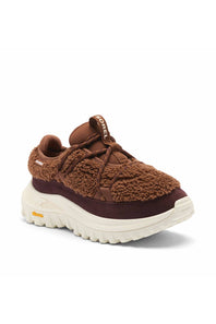 A brown textured sneaker with a chunky off-white sole, featuring a fuzzy sherpa-like upper, dark brown suede overlays, and a small yellow Vibram logo on the side.
