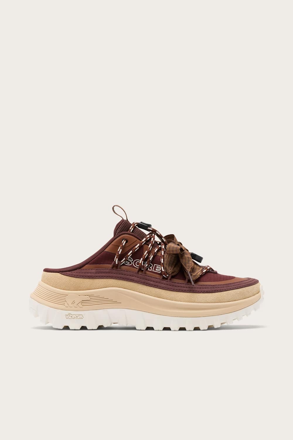 A single low-top sneaker shown in side profile against a light off-white background. The shoe features a dark brown suede upper with a matching brown lace, a thick beige midsole, and a white lug sole.