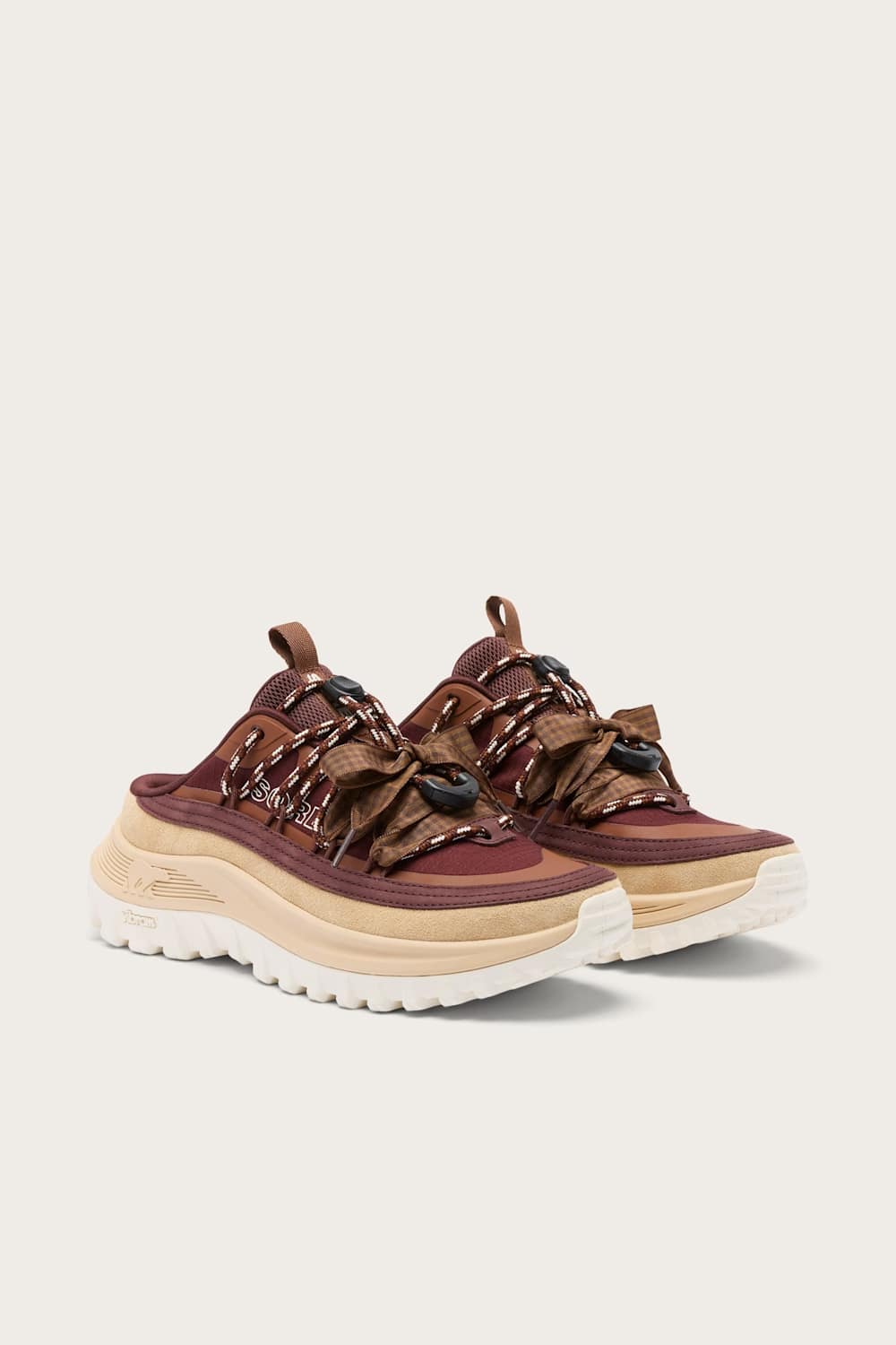 A pair of chunky platform sneakers in brown and burgundy with textured brown straps and thick beige and white soles, shown against a light beige background.