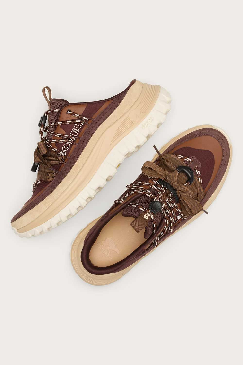 A pair of brown and beige chunky platform sneakers with brown laces threaded through metal eyelets, shown from a top-down view on a light beige background.