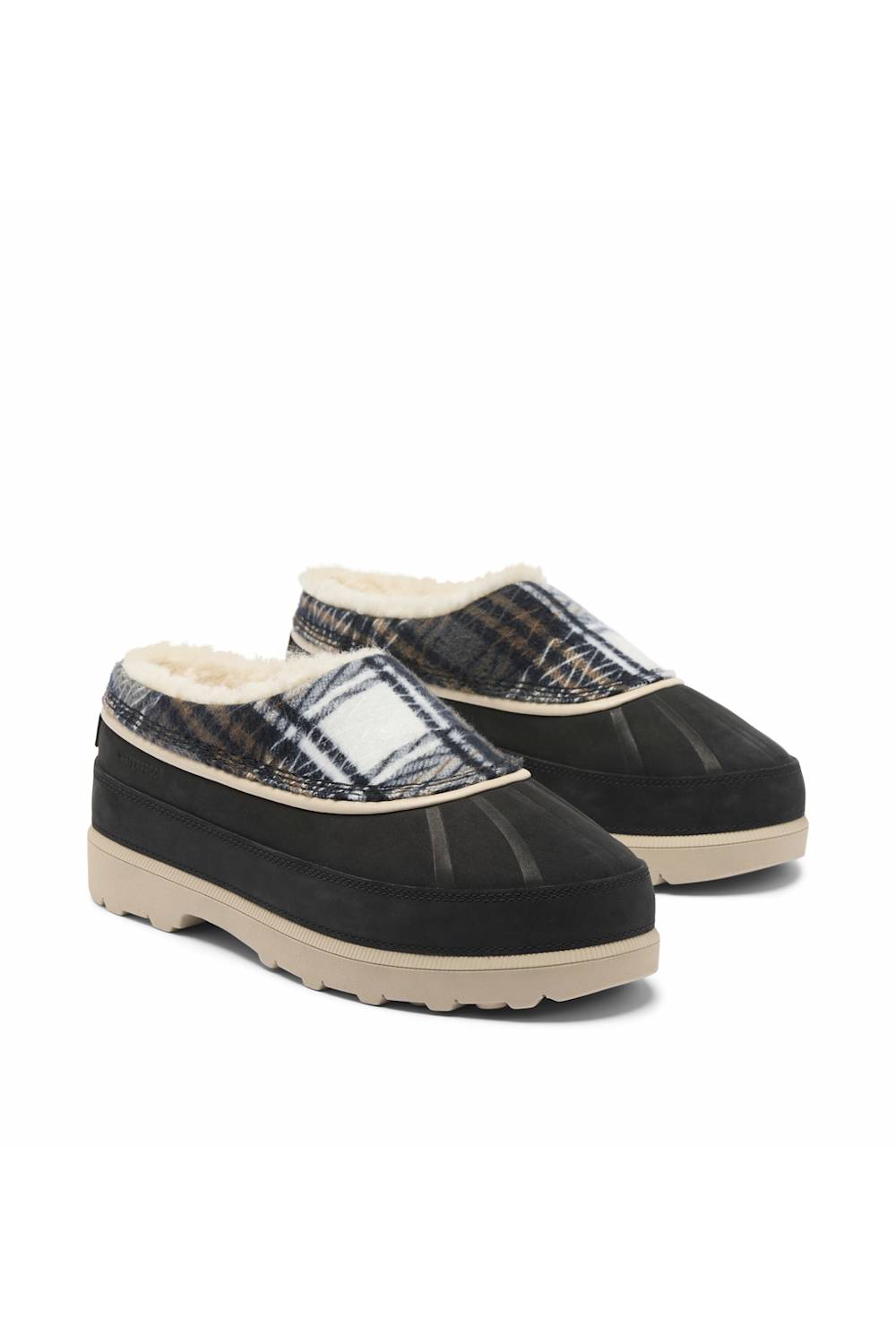 A pair of slip-on mule slippers with a black suede-like toe and heel, a navy and beige plaid pattern across the upper, and a cream-colored fleece lining and sole.