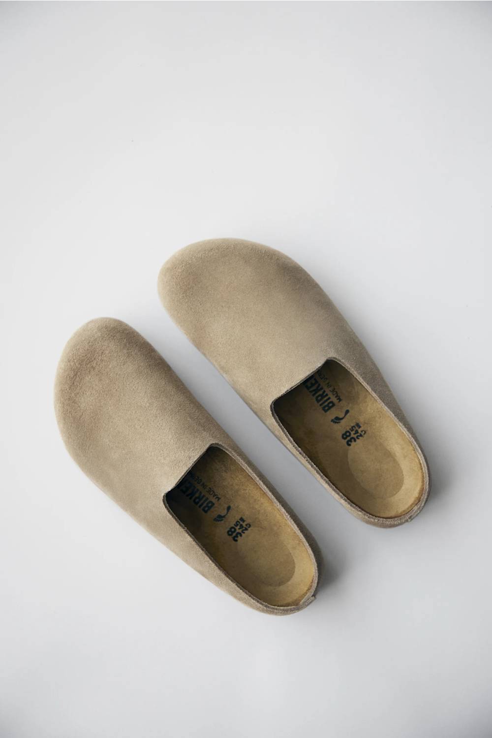 A pair of taupe suede slip-on loafers shown from a top-down view on a light gray background.