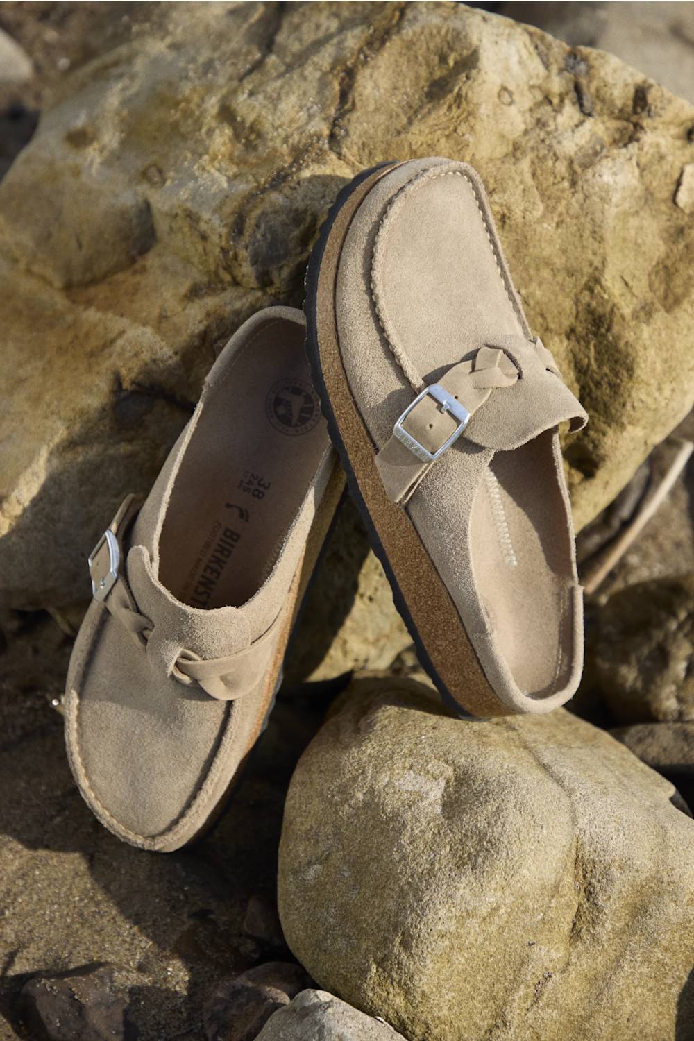 Pair of brown suede shoes with buckles on a rocky surface