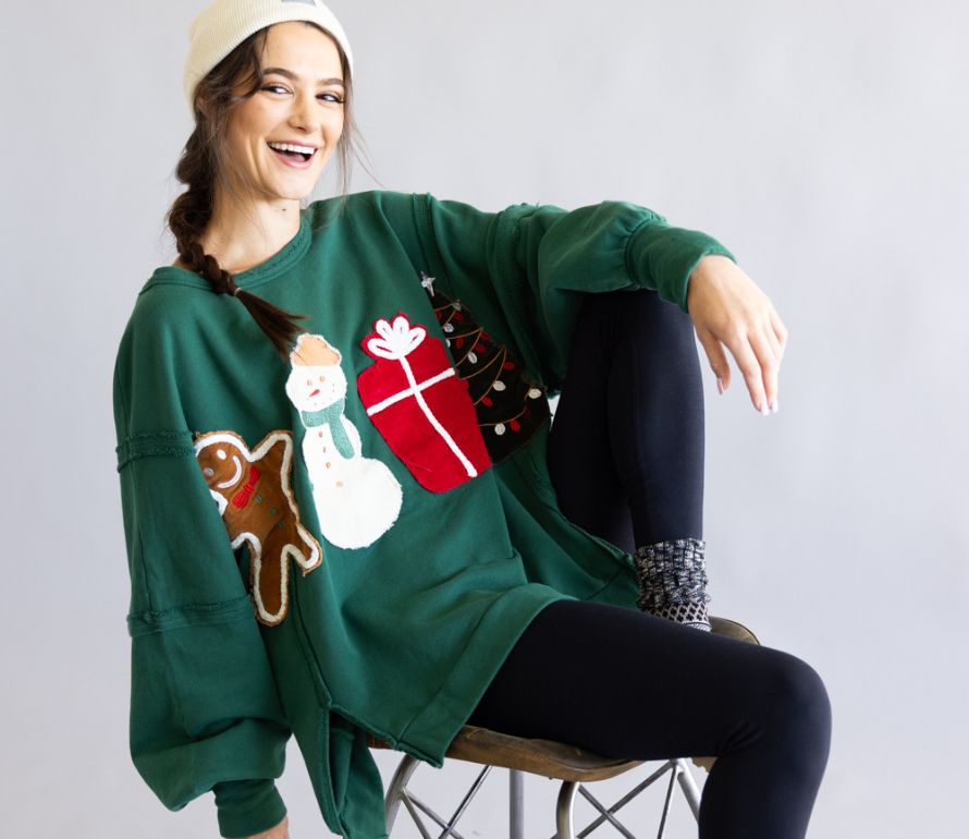 Woman wearing a green Christmas-themed sweater with a snowman, gingerbread man, and gift design.