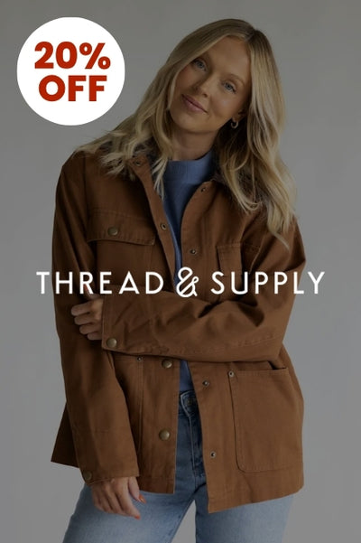 Promotional graphic with a woman wearing a brown barn jacket and denim jeans in front of a basic background with an image overlay darkening the image. The Thread & Supply logo in white is in the center of the image and a circular callout in the upper left corner that reads 20% OFF