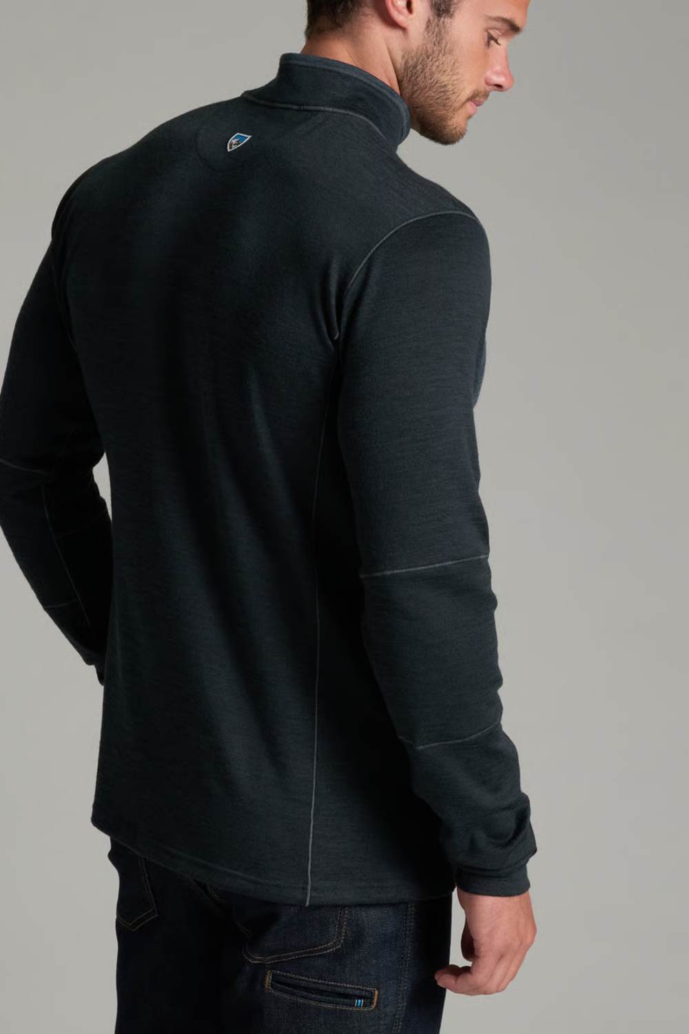 A man wearing a dark charcoal gray quarter-zip fleece pullover, shown from a three-quarters back view against a solid gray studio background.