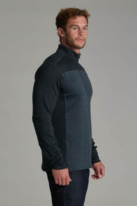 A man wearing a dark gray and black color-blocked quarter-zip fleece pullover, shown from a side profile against a solid gray studio background.