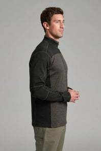 A man in side profile wearing a color-blocked quarter-zip fleece pullover with dark charcoal and heather gray panels, paired with khaki pants, against a solid gray studio background.