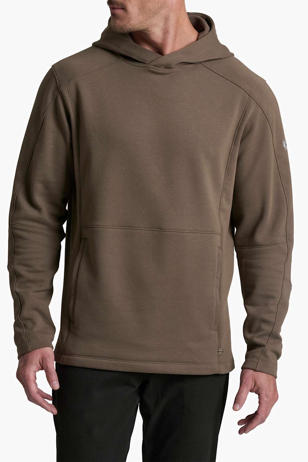A man wearing a brown hooded sweatshirt with a kangaroo pocket, paired with black pants, shown from the chin down against a light gray background.