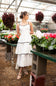 Open Back Tiered Midi Dress for Women in Off White; Woman in a white dress standing in a greenhouse with potted plants.