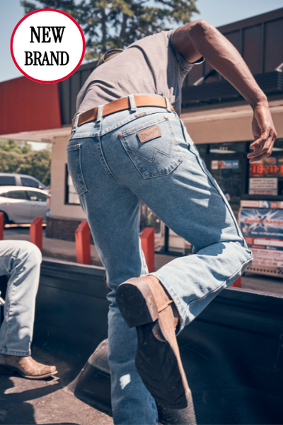 Man in light blue jeans and brown boots climbing into truck, with a 