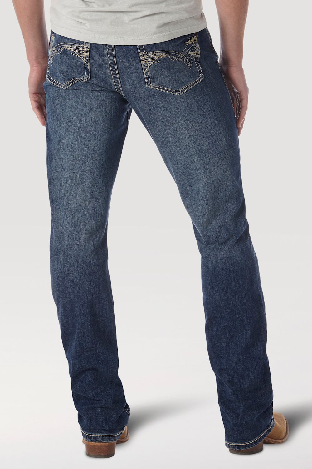 Rear view of a person wearing dark blue denim jeans with contrast stitching and tan boots against a light gray studio background.